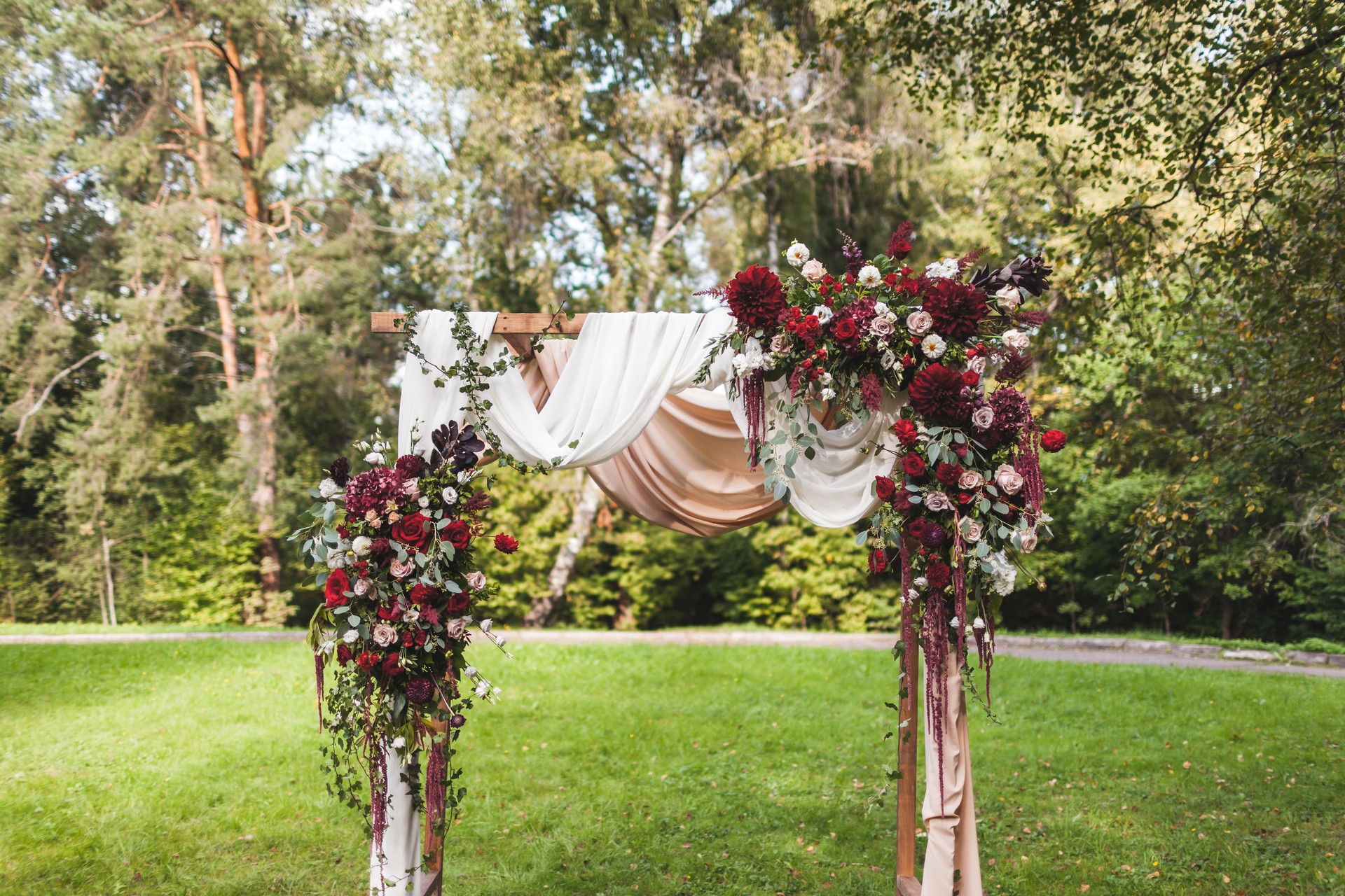 Wedding ceremony in rustic style decorated with different red flowers, white textile and chairs in forest